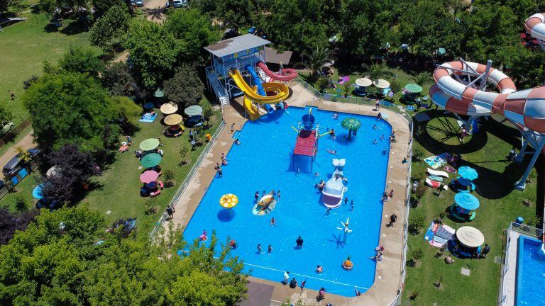 La piscina Acuafly rodeada de césped y árboles, con los toboganes del parque al fondo