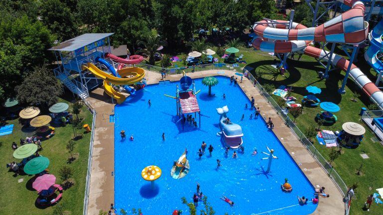 Bañistas en la piscina Acuafly, con los toboganes de colores detrás