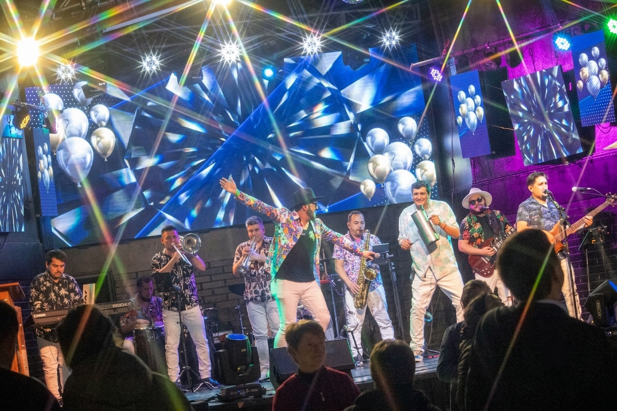 Banda tocando en vivo en un escenario con luces y globos